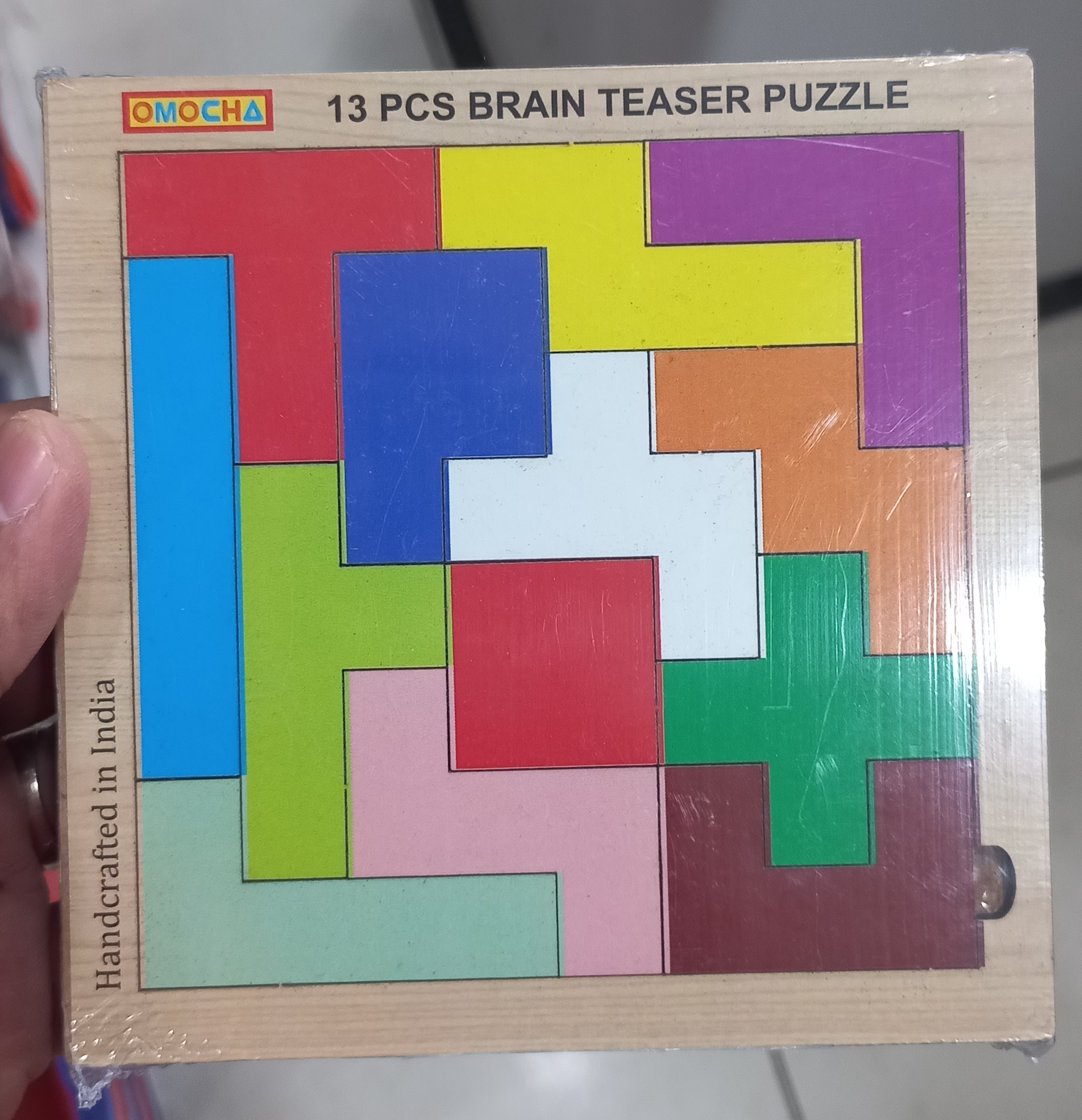 A 13-piece wooden brain-teaser puzzle, all pieces packed into a square tray