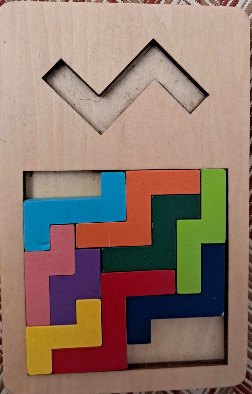 A wooden puzzle with a zigzag mountain-shaped cavity to fill with tetromino-like pieces