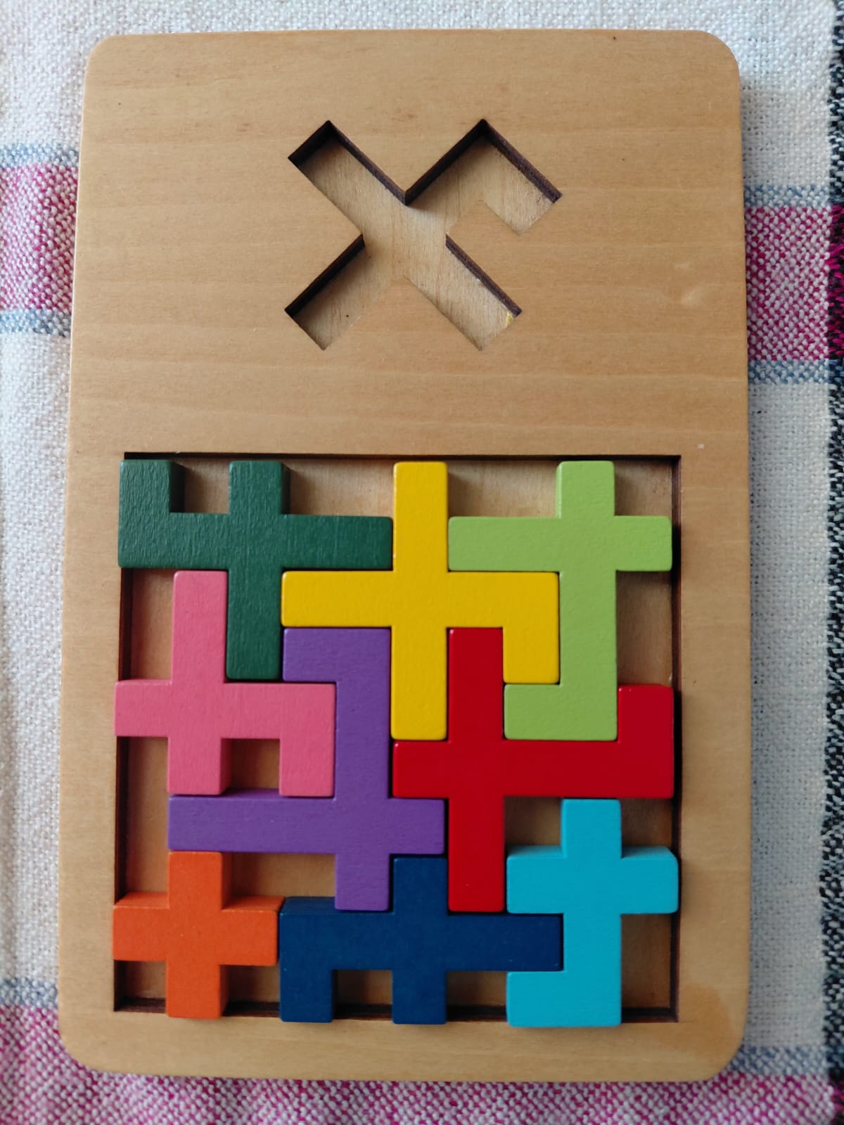 A wooden puzzle made of plus-sign pieces packed into a tray with an X-shaped cavity
